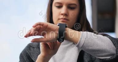年轻的女人在街上用他的智能手表。 风吹拂着她的头发。 智能手表，苹果，时间4k
